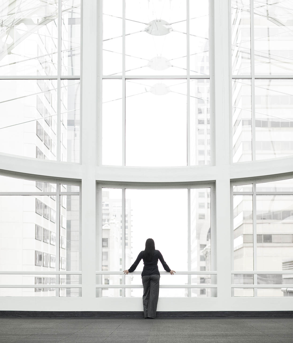 A businesswoman is standing at a window in a large convention center lobby.